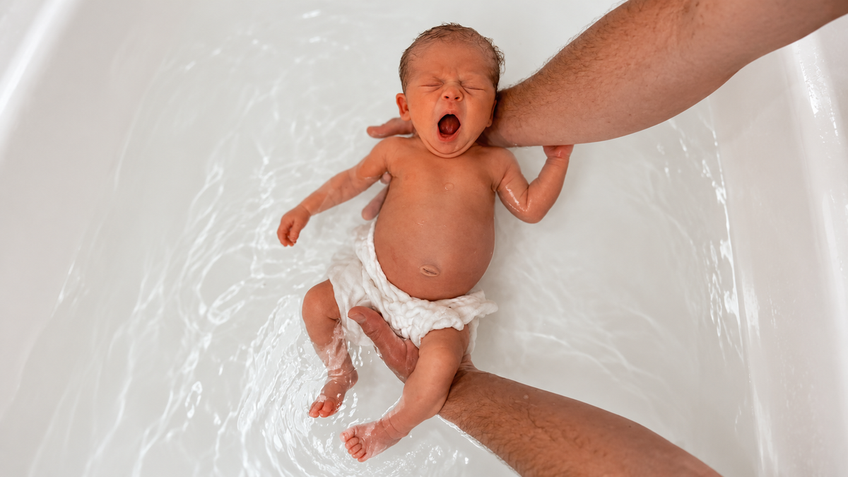 Newborn in the bath wrapped in a 3 Little Crowns organic cotton gauze cloth